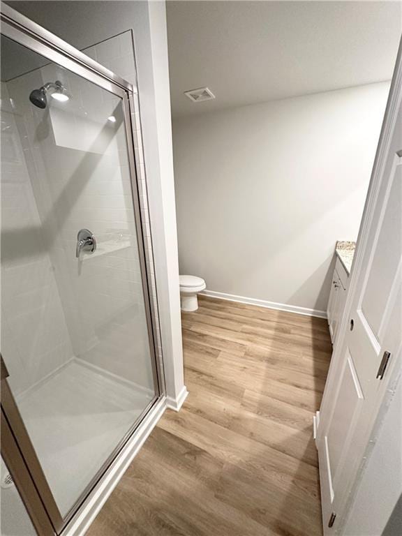 full bathroom with wood finished floors, a stall shower, toilet, vanity, and baseboards