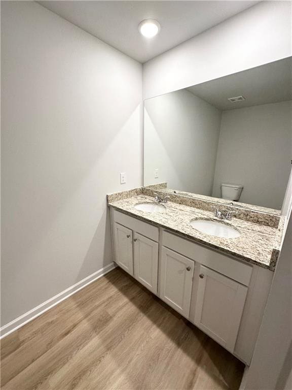 bathroom featuring wood finished floors, toilet, double vanity, and baseboards