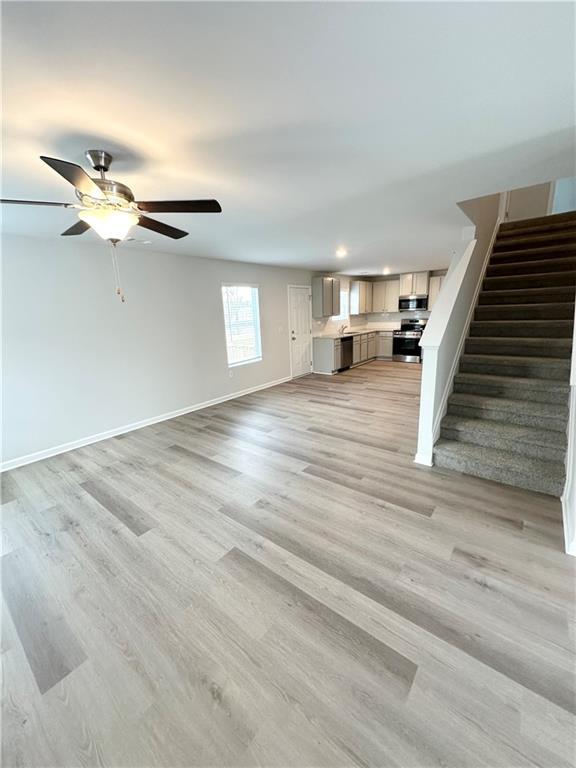 unfurnished living room with stairway, a ceiling fan, light wood finished floors, baseboards, and recessed lighting