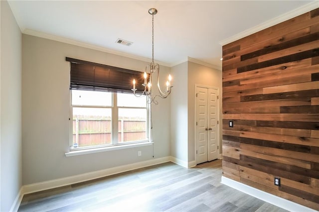 unfurnished dining area featuring a notable chandelier, baseboards, ornamental molding, visible vents, and wood finished floors