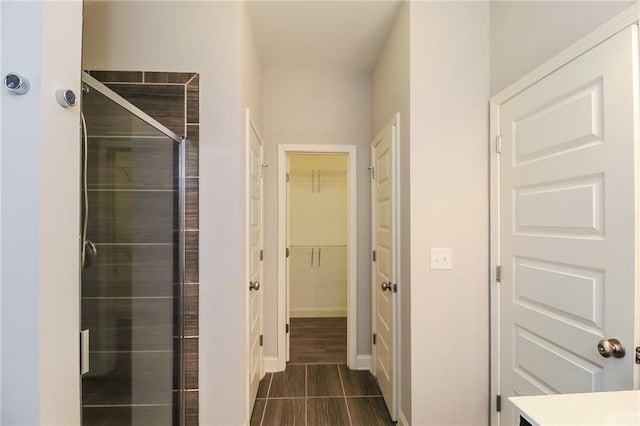 bathroom featuring a walk in closet, baseboards, and a shower stall