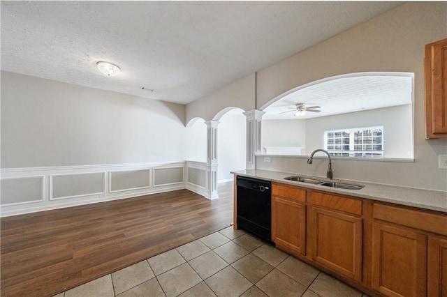 kitchen featuring brown cabinetry, light tile patterned flooring, decorative columns, a sink, and black dishwasher