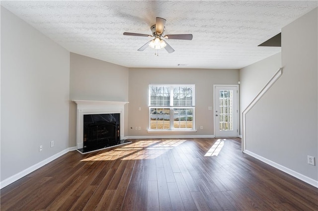 unfurnished living room with a textured ceiling, a high end fireplace, baseboards, ceiling fan, and dark wood-style flooring