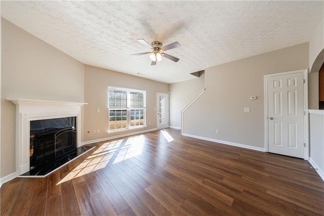 unfurnished living room featuring wood finished floors, baseboards, a fireplace, ceiling fan, and a textured ceiling