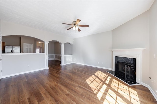 unfurnished living room with a high end fireplace, decorative columns, wood finished floors, arched walkways, and a ceiling fan