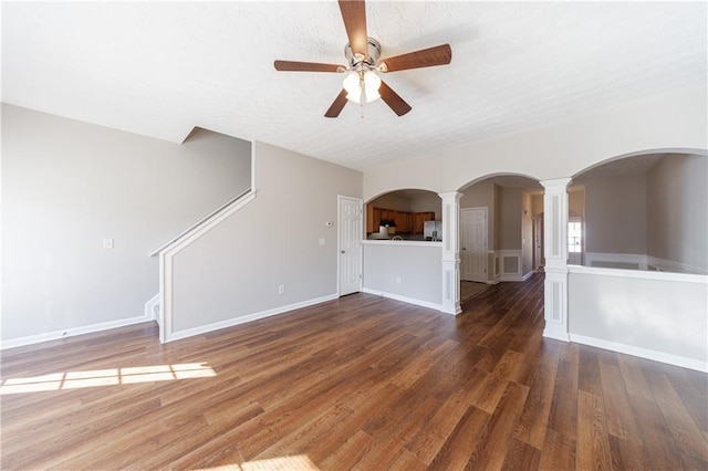 unfurnished living room featuring ornate columns, arched walkways, ceiling fan, and wood finished floors