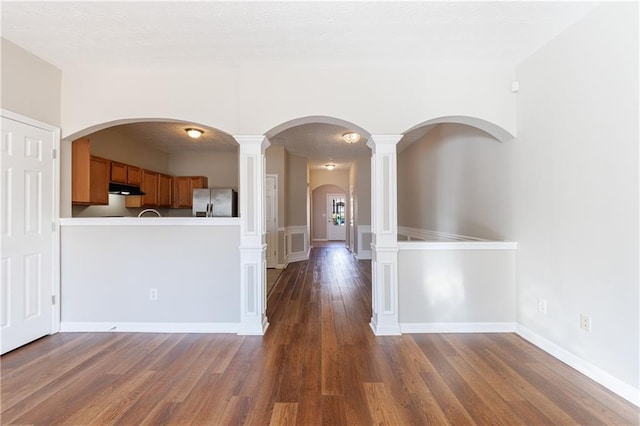 interior space with arched walkways, baseboards, and wood finished floors