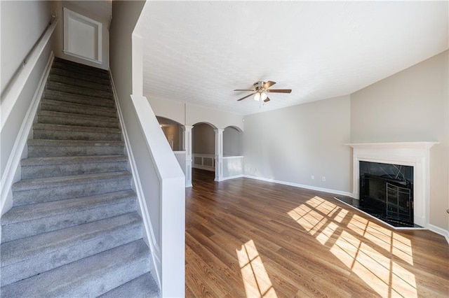 staircase featuring a high end fireplace, wood finished floors, arched walkways, a textured ceiling, and a ceiling fan