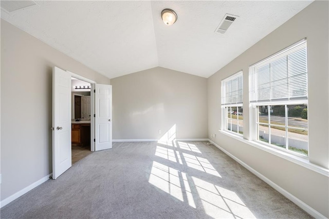 empty room with light colored carpet, vaulted ceiling, baseboards, and visible vents