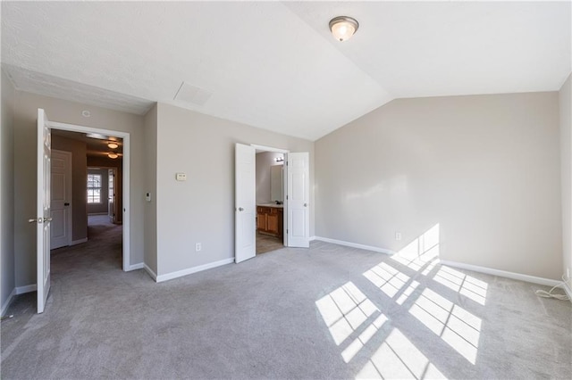 unfurnished bedroom featuring light carpet, ensuite bath, baseboards, and vaulted ceiling