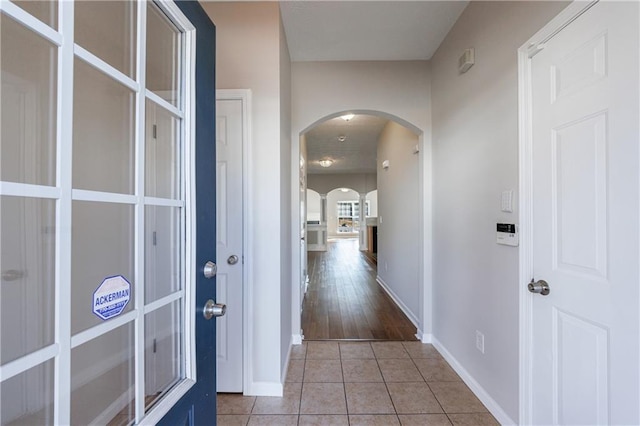 hall featuring light tile patterned floors, baseboards, and arched walkways