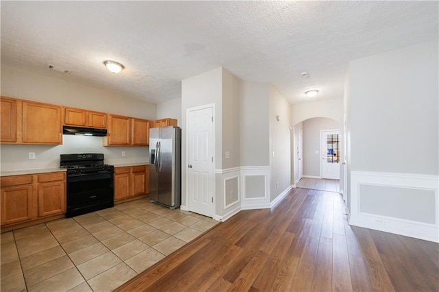 kitchen with gas stove, arched walkways, light countertops, stainless steel fridge, and light wood-type flooring