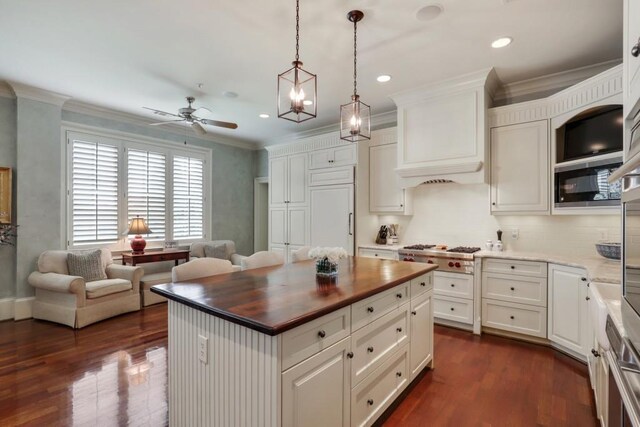 kitchen featuring built in appliances, decorative light fixtures, a kitchen island, ceiling fan with notable chandelier, and dark hardwood / wood-style flooring