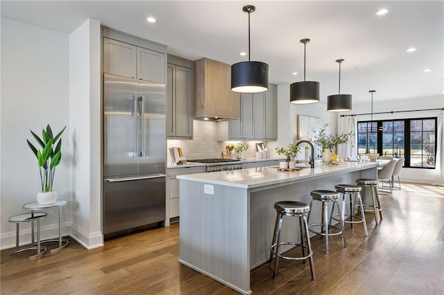 kitchen featuring a kitchen breakfast bar, light countertops, an island with sink, stainless steel built in refrigerator, and pendant lighting