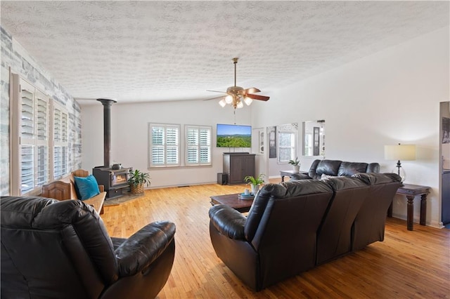 living area with lofted ceiling, ceiling fan, a textured ceiling, hardwood / wood-style floors, and a wood stove