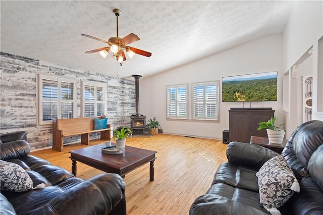 living room with a wood stove, hardwood / wood-style floors, a textured ceiling, and lofted ceiling