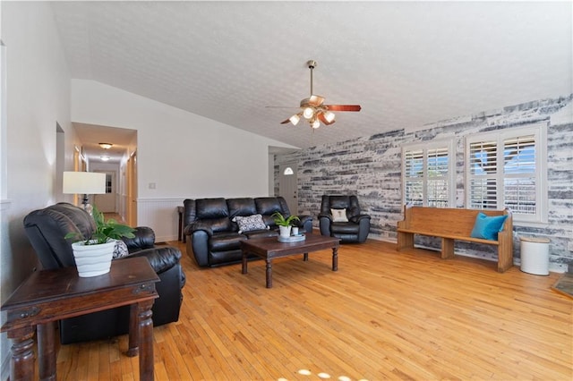 living area with lofted ceiling, light wood finished floors, ceiling fan, and a textured ceiling