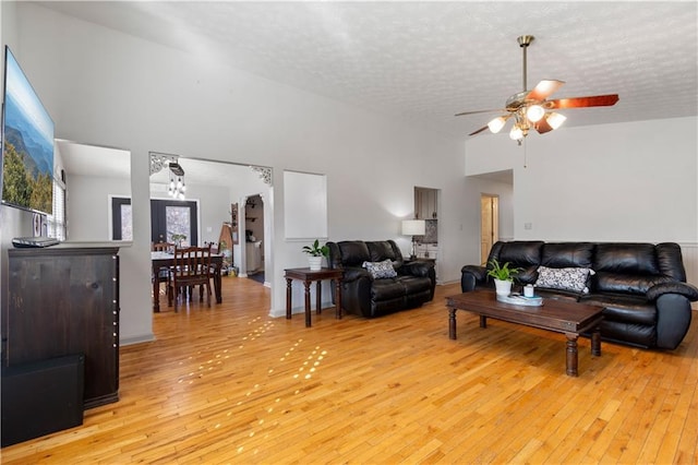 living room featuring a textured ceiling, high vaulted ceiling, light wood-style flooring, and a ceiling fan