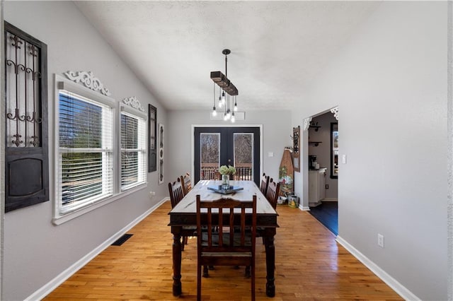 dining room with french doors, light wood finished floors, lofted ceiling, visible vents, and baseboards