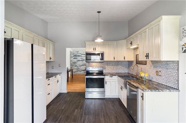 kitchen featuring dark stone counters, appliances with stainless steel finishes, dark wood-style flooring, cream cabinets, and a sink