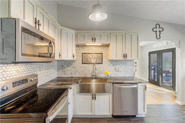 kitchen featuring dark wood-type flooring, a sink, appliances with stainless steel finishes, tasteful backsplash, and dark stone countertops