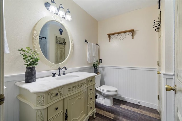 bathroom with toilet, vanity, wood finished floors, and wainscoting