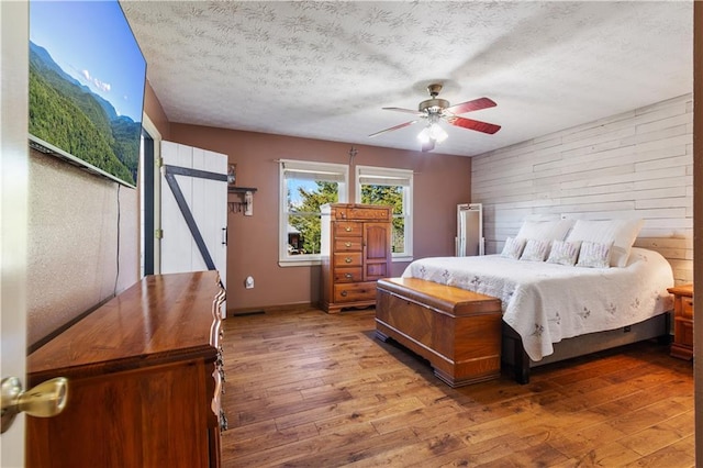 bedroom featuring a textured ceiling, ceiling fan, wooden walls, an accent wall, and hardwood / wood-style floors