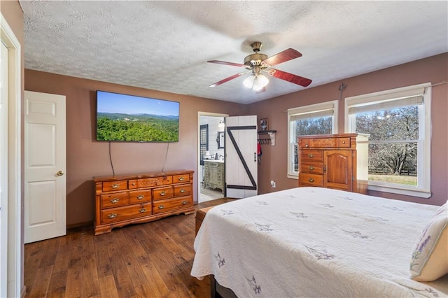 bedroom featuring a textured ceiling, dark wood-style flooring, ensuite bath, and a ceiling fan