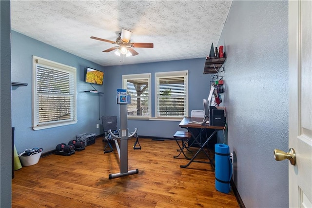 exercise area featuring a ceiling fan, plenty of natural light, a textured ceiling, and wood finished floors