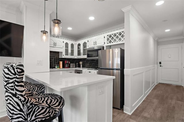 kitchen featuring kitchen peninsula, crown molding, appliances with stainless steel finishes, a kitchen bar, and white cabinetry