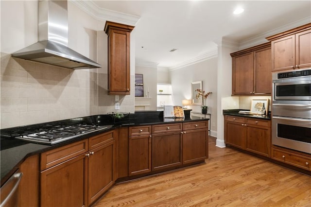 kitchen featuring wall chimney range hood, stainless steel appliances, dark stone countertops, ornamental molding, and light hardwood / wood-style flooring