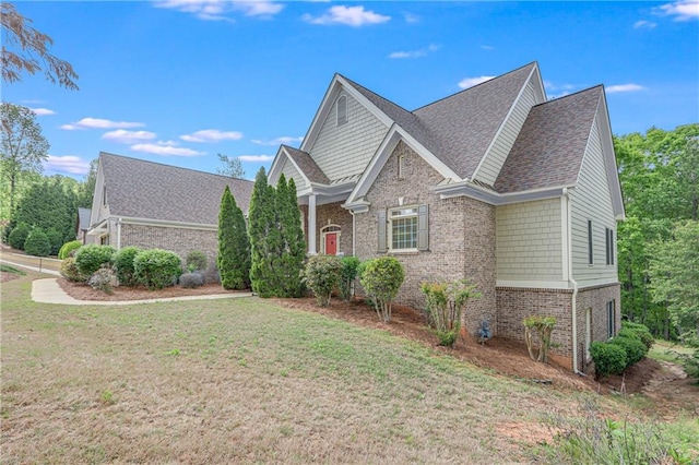 view of side of home with brick siding, a lawn, and a shingled roof