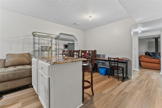 kitchen featuring white cabinetry, light hardwood / wood-style floors, a breakfast bar, and stone countertops