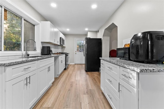 kitchen featuring sink, white cabinetry, backsplash, light stone counters, and black appliances