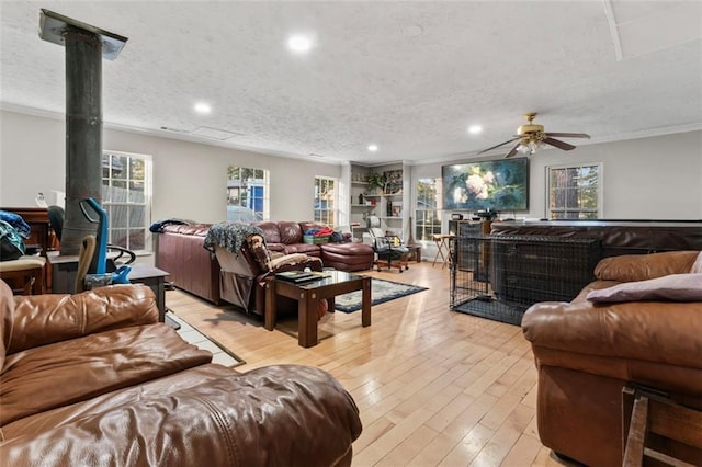 living room with a wood stove, light hardwood / wood-style floors, crown molding, plenty of natural light, and a textured ceiling