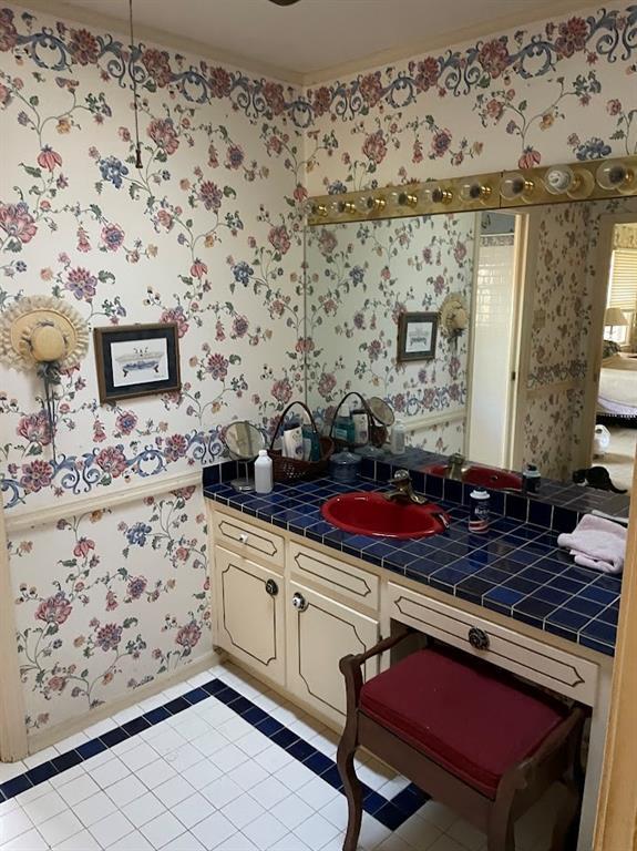 kitchen featuring tile patterned floors, a sink, cream cabinets, tile countertops, and wallpapered walls