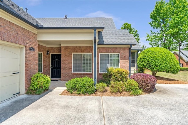 property entrance featuring brick siding, roof with shingles, and concrete driveway