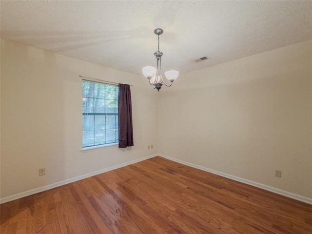 empty room with a chandelier, wood finished floors, and baseboards