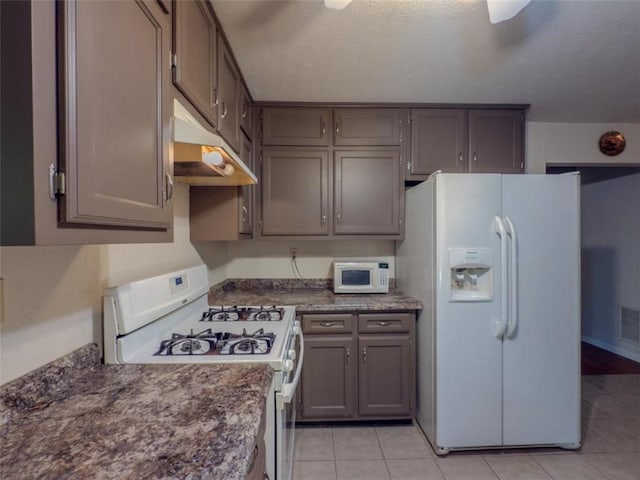 kitchen with white appliances, under cabinet range hood, dark countertops, light tile patterned floors, and gray cabinets
