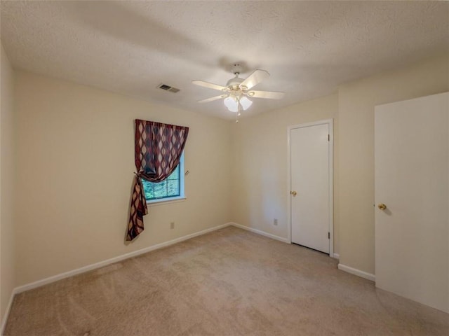 empty room with light carpet, ceiling fan, baseboards, and a textured ceiling