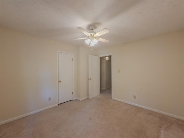 unfurnished room with a ceiling fan, light colored carpet, baseboards, and a textured ceiling