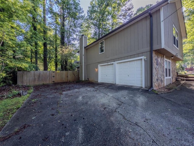 view of side of property with fence, a chimney, a garage, stone siding, and driveway