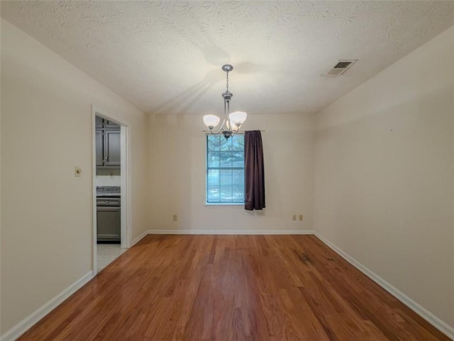 empty room with wood finished floors, a chandelier, baseboards, and a textured ceiling