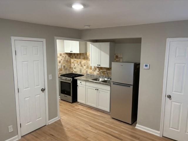 kitchen featuring light wood-type flooring, refrigerator, stainless steel gas range, sink, and white cabinetry