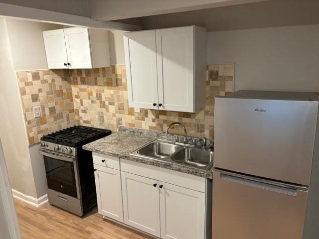 kitchen with white cabinets, white refrigerator, stainless steel range with gas cooktop, and sink