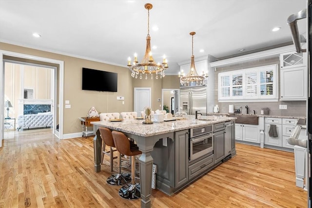 4670 Hamden Forest Dr SW, Atlanta, GA 30331 - kitchen featuring a chandelier, ornamental molding, appliances with stainless steel finishes, a center island with sink, and light wood-type flooring