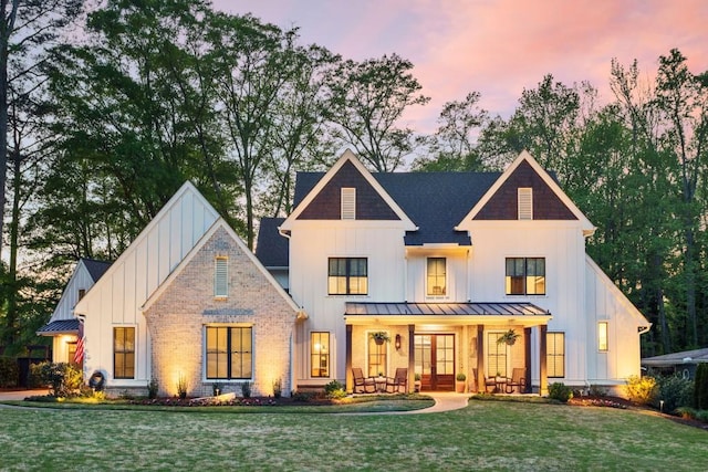 rear view of house with board and batten siding, a lawn, a standing seam roof, and a porch