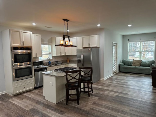 kitchen featuring a center island, hanging light fixtures, appliances with stainless steel finishes, stone countertops, and a kitchen bar