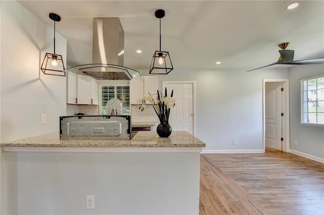 3991 Adamsville Dr SW, Atlanta, GA 30331 - kitchen with island exhaust hood, light wood-type flooring, a peninsula, white cabinetry, and light stone countertops