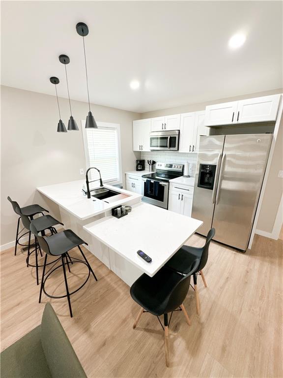 kitchen featuring decorative light fixtures, light hardwood / wood-style floors, stainless steel appliances, and white cabinetry